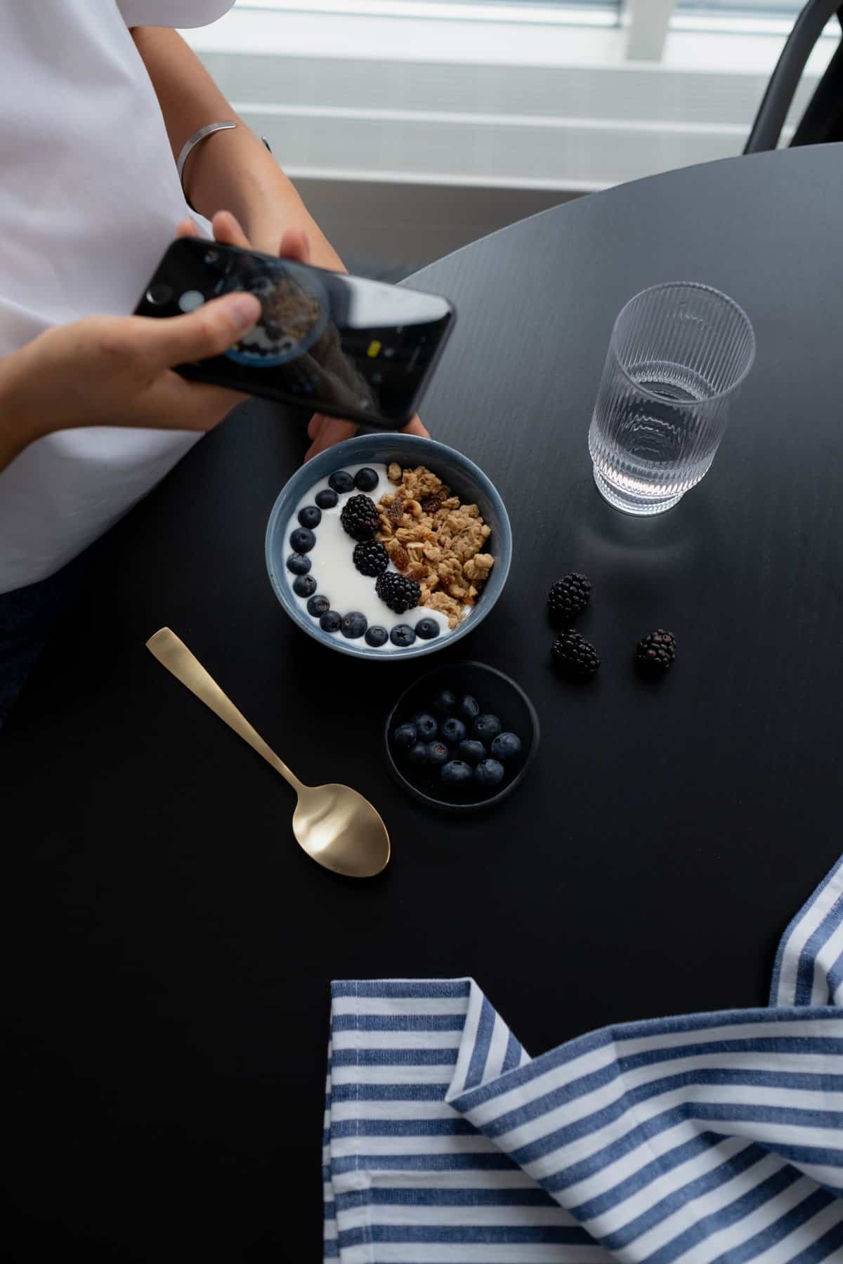 Free Woman Taking Photo Of Granola With Blueberries In A Bowl On Black Table Stock Photo