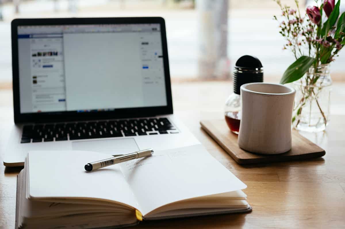 An open notebook with a cup of coffee and a laptop.