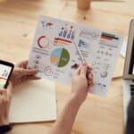 Free Team Members Analyze Charts During A Business Meeting With Laptops And Smartphones. Stock Photo