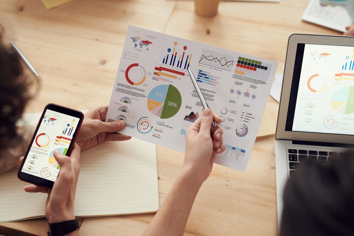 Free Team Members Analyze Charts During A Business Meeting With Laptops And Smartphones. Stock Photo